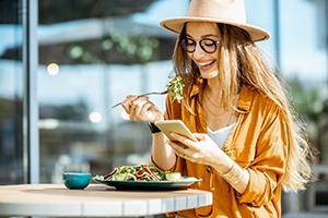 Smiling woman enjoying lunch while looking at phone